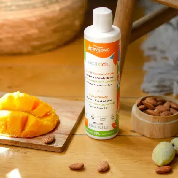 Un flacon d'après-shampooing Activilong Paris Ti Après-Shampooing Actikids 250 ml est présenté sur une surface en bois à côté de mangues tranchées et d'amandes entières. dakar