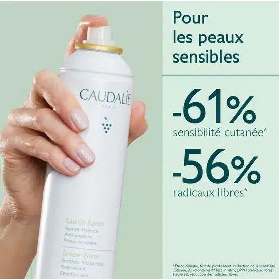 Gros plan d'une main tenant une canette de spray d'eau de raisin « Caudalie Eau de Raisin Apaisante