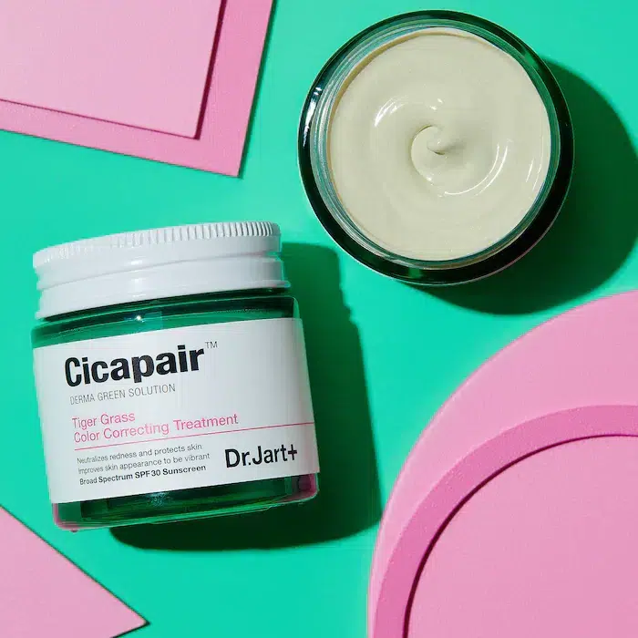 Pot de Crème Traitement Anti Rougeur et Imperfections Dr Jart+ Cicapair Tiger Grass avec une crème tourbillonnée à côté sur un fond géométrique vert et rose. dakar