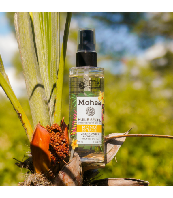 Un flacon de MKL Huile sèche - Monoï - 100 ml est niché au milieu d'un feuillage tropical avec un fond naturel flou