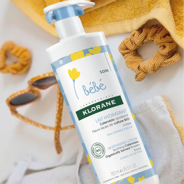 Un flacon de KLORANE Lait hydratant au Calendula 750 ml est posé sur une serviette à côté des accessoires pour bébé. dakar