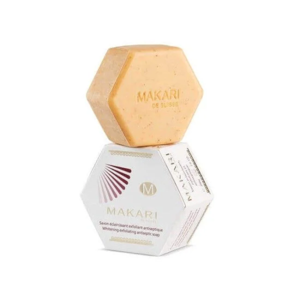 Barre de savon orange hexagonale étiquetée « Makari Brightening Savon Éclaircissant Exfoliant 200 g » sur une boîte blanche hexagonale avec logo et marque Makari.