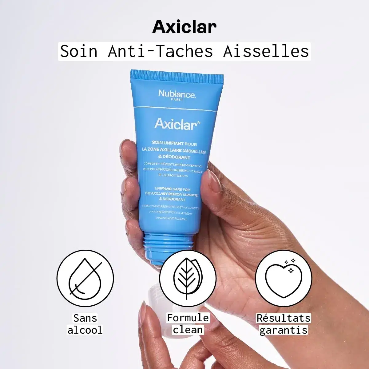 Une personne tenant un tube bleu de produit de soin des aisselles Nubiance Axiclar Soin Anti Taches Aisselles 75 ml avec des icônes et du texte indiquant ses caractéristiques ci-dessous. dakar