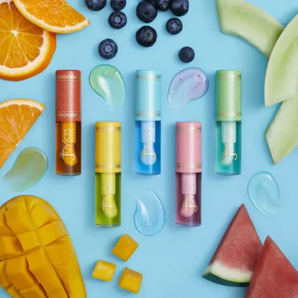 Tubes de baume à lèvres vibrants en orange, jaune, bleu, violet et vert sur fond bleu, entourés de tranches d'orange, de mangue, de pastèque, de melon miel et de myrtilles, avec des échantillons de gel assortis. Dakar