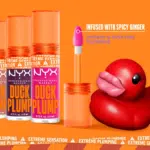 Un fond orange vif avec trois tubes de brillant à lèvres « Duck Plump » de NYX Professional Makeup, avec un tube ouvert et audacieux doté d'un applicateur. Un canard en caoutchouc rouge aux lèvres exagérées se trouve à droite, sous un texte sur l'infusion de gingembre épicé. Dakar